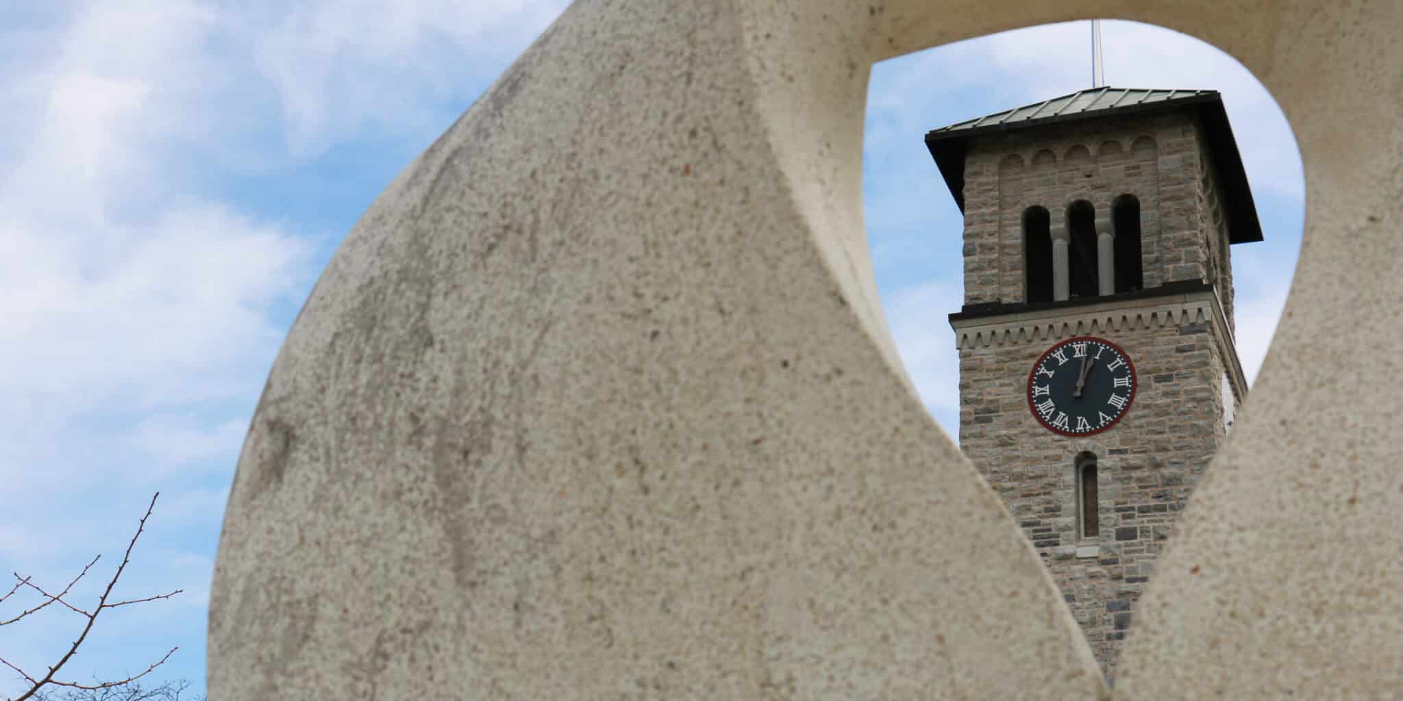 Image of a clocktower framed and shot through the opening of a stone sculpture.