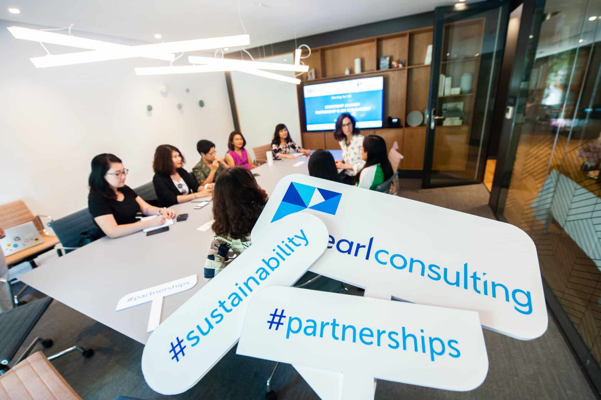 Image of the Pearl Consulting team sitting around a boardroom table with signage reading #sustainability and #partnerships.