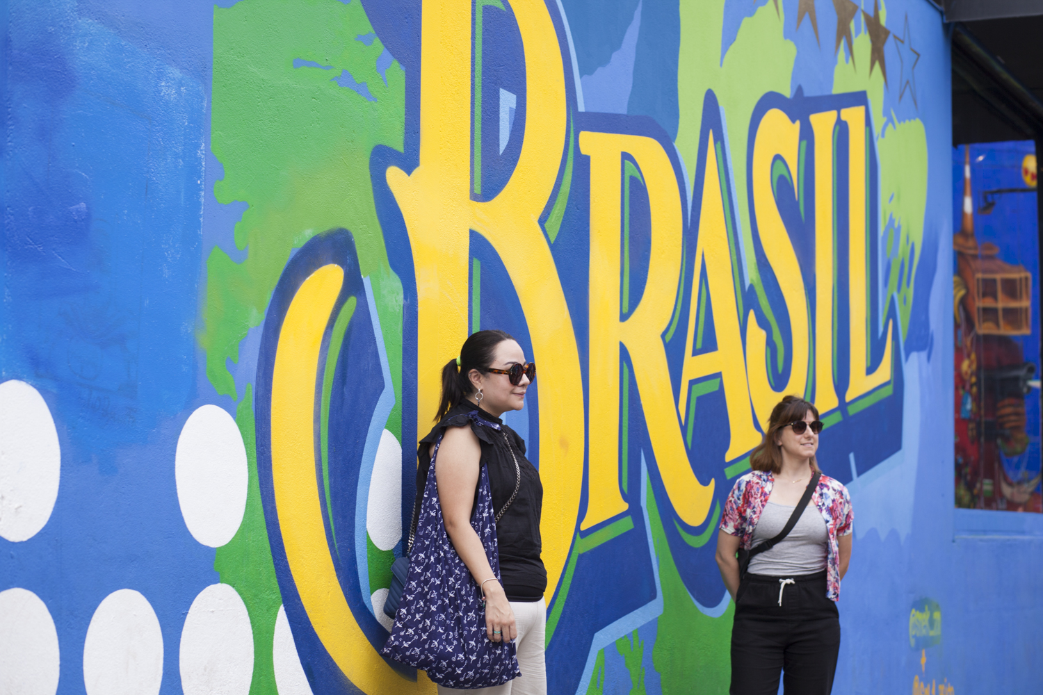 Two people standing in front of a vibrant mural with the word 'Brasil'.